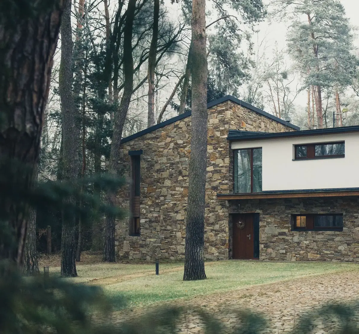 Casa com base em pedra e volume rebocado a branco, entre pinheiros, com luz natural