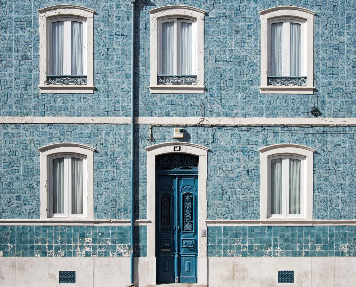 Fachada revestida a azulejo azul com janelas de guilhotina e porta de madeira