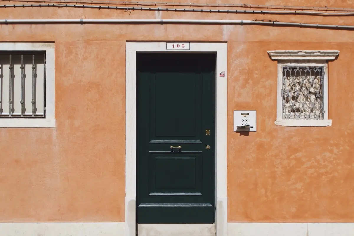 Fachada de reboco cor de laranja com porta verde e janela gradeada