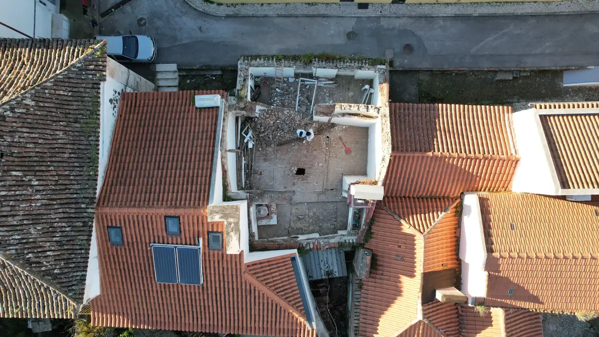 Largo D. Dinis visto de drone: telhados de telha e o edifício em obra, sem cobertura, no centro do quarteirão